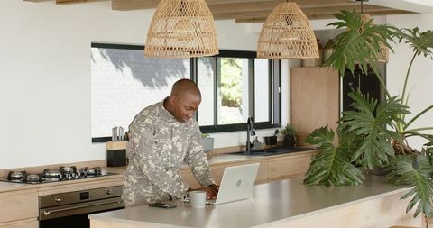 Military professional engaging in remote work in modern kitchen