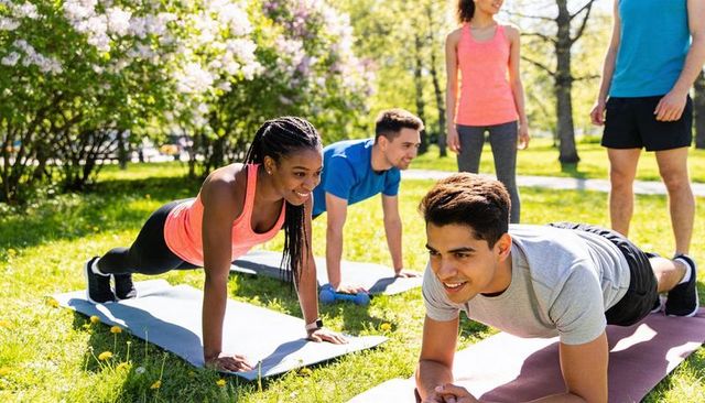 Diverse group performing plank workout on grassy park lawn sunny outdoor fitness training