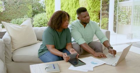 Couple managing finances at home using laptop and tablet
