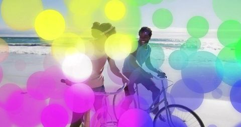Couple riding cruiser bikes along sunny beach with colorful bokeh overlays