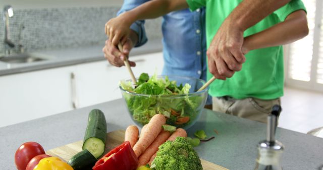 Father and daughter preparing a healthy salad together in a modern kitchen, showcasing fresh vegetables on a cutting board. Perfect for illustrating family bonding, healthy eating habits, and home cooking. Suitable for use in articles, advertisements, and blogs about nutrition, family time, and cooking at home.