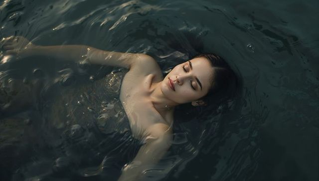 Serene woman floating on dark water with eyes closed and wet hair fanning around