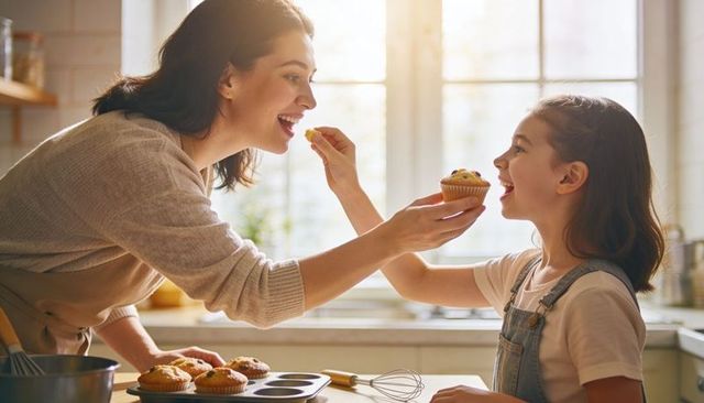 Mother and daughter tasting warm muffins together in sunlit cozy kitchen during morning bake