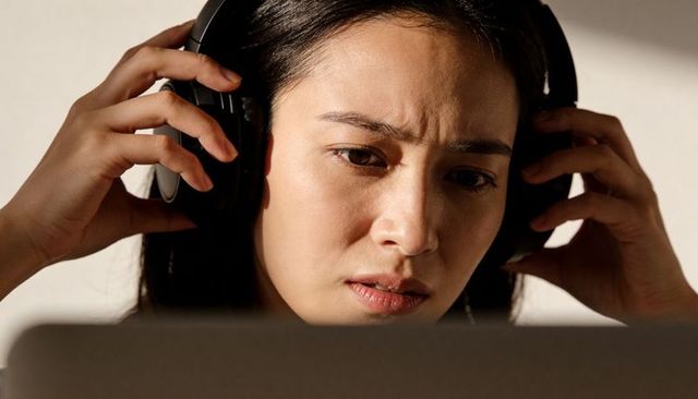 Asian woman adjusting headphones while concentrating on laptop closeup