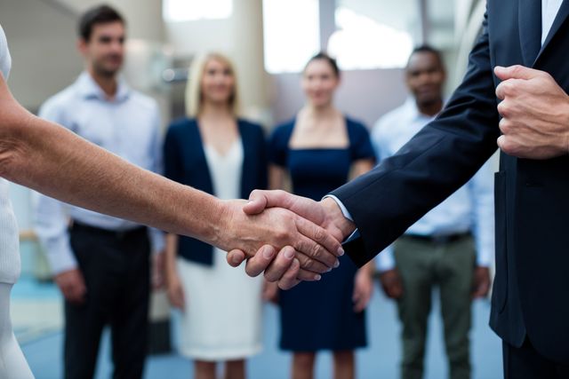 Business professionals making a handshake in a conference center, symbolizing agreement and cooperation. Ideal for use in business articles, corporate websites, marketing materials, and presentations depicting partnership, teamwork, networking, and successful deals.