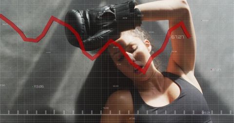 Exhausted female boxer lying on mat pressing glove to head with falling red data chart