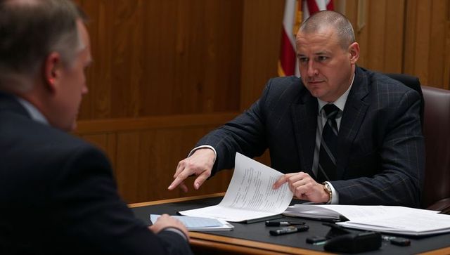 Courtroom hearing attorney pointing while reviewing legal documents at wood-paneled bench