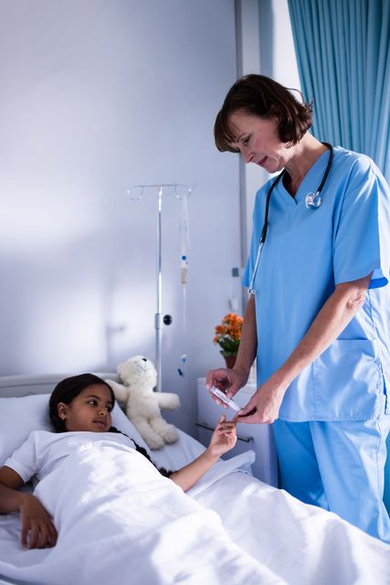 Female doctor in blue scrubs checking the sugar level of a young patient lying in a hospital bed. The scene includes medical equipment such as an IV drip and a stethoscope, indicating a professional healthcare environment. This image is ideal for use in healthcare-related content, medical websites, pediatric care promotions, and educational materials about hospital care.