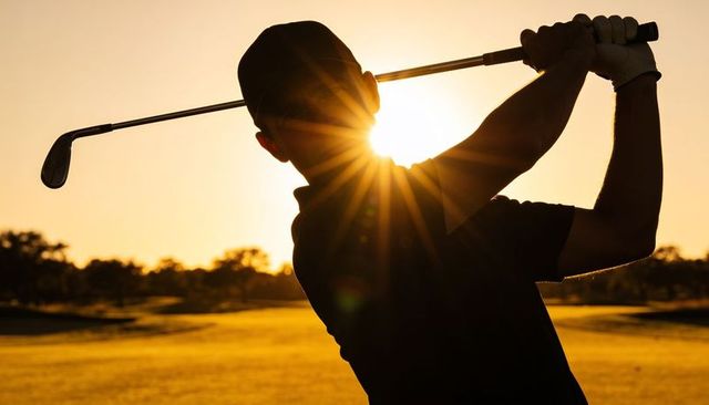 Sunburst silhouette golfer following through on sunset fairway with club
