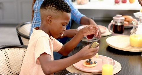 Boy Pouring Honey on Pancakes at Family Dining Table