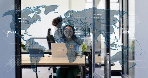Female professional working on laptop with headset in glass office global data map overlay