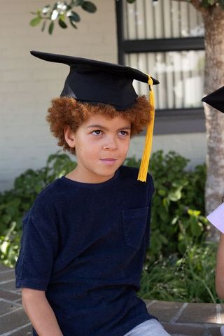 African american child wearing graduation cap with yellow tassel sitting on school bench