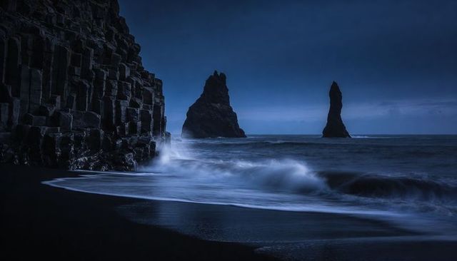 Midnight basalt cliffs with towering sea stacks over black sand beach, twilight seascape