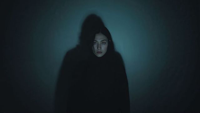 Standing Asian woman blending into shadow with spotlight creating moody low-key portrait