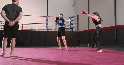 Female boxers sparring under coach supervision in gym training session, focused