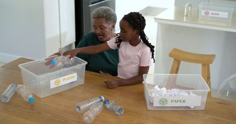 African American Grandmother Teaching Granddaughter to Sort Recycling at Kitchen Table