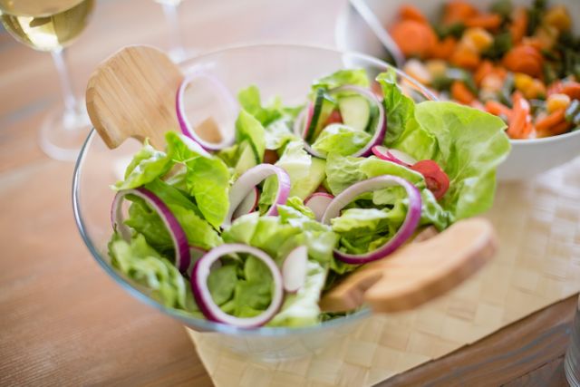 Fresh green salad with lettuce and onions in a glass bowl on a dining table. Ideal for illustrating healthy eating, vegetarian meals, and home dining settings. Perfect for use in food blogs, nutrition articles, and healthy lifestyle promotions.