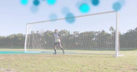 Goalkeeper standing in net holding soccer ball during training on sunny grass pitch