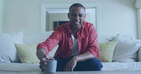Cheerful Man in Casual Attire Reaching for Mug in Cozy Living Room