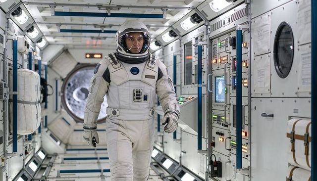 Astronaut walking through spacecraft corridor wearing white EVA helmet and suit during mission