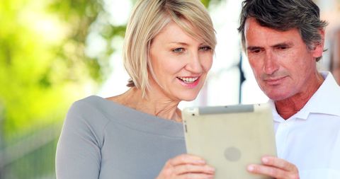 Smiling Mature Business Professionals Collaborating on Tablet Outdoors