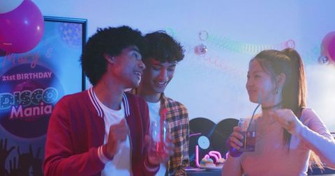 Diverse friends dancing and chatting at neon disco birthday party with retro vinyl decor