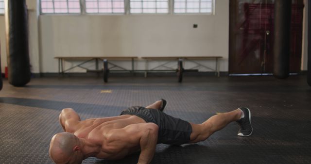 Caucasian muscular shirtless bald man exercising, doing push ups. health and fitness training at gym.