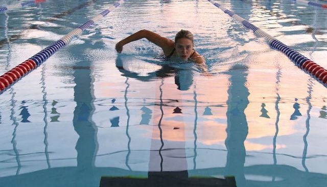 Competitive female swimmer performing freestyle in lane with pastel reflections and ripples