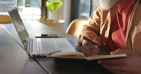 Senior Man in Thought Writing at Home Desk with Laptop