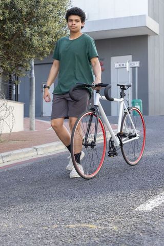 Young man walking with urban road bike featuring red front rim on city street