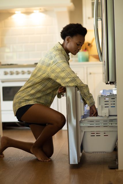 African American woman opening the fridge freezer in the kitchen at home. Domestic life and spending time at home. 