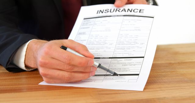Close-up of a hand signing an insurance contract document with a pen. Ideal for illustrating themes related to insurance, legal agreements, business contracts, paperwork, and financial protection.