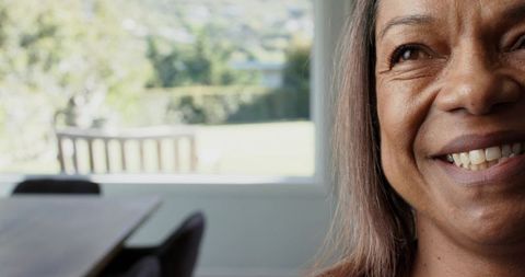 Warm closeup of mature woman smiling by sunlit window in modern dining room