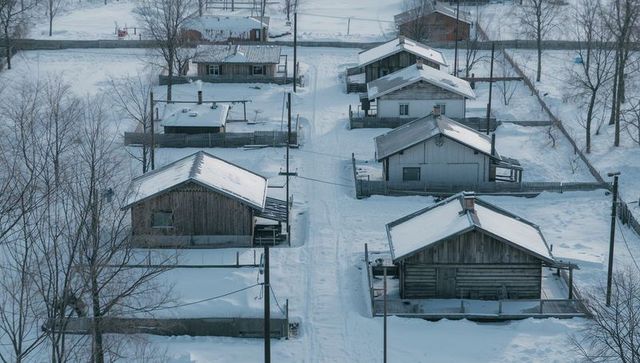 Aerial view snow-covered wooden cabins lining quiet rural winter lane