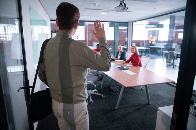 Rear view of businessman walking into meeting room and greeting colleagues. working in business at a modern office.