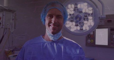 Smiling surgeon standing under surgical lights in operating room wearing blue scrubs
