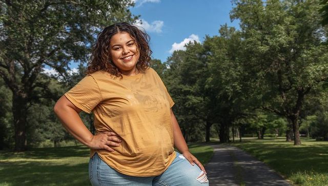 Smiling curvy woman walking on sunny park path wearing mustard tee and ripped jeans