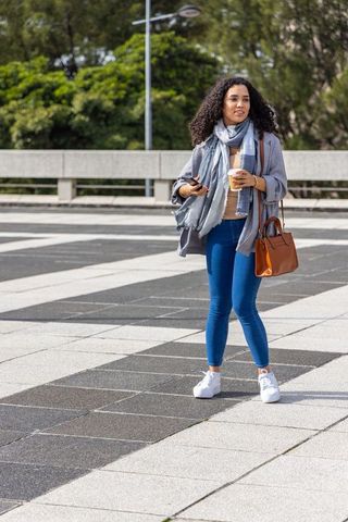City woman walking with coffee and smartphone wearing scarf and coat, casual street style