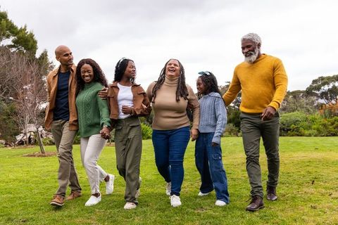 Multigenerational african american family walking laughing together in park wearing sweaters and jea