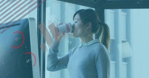 Asian professional woman sipping coffee by glass wall with digital gauges in modern office