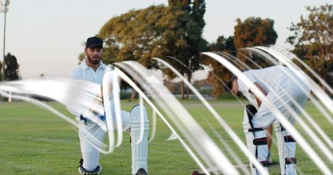 Kneeling cricketers adjusting pads near crease during golden hour training