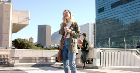 Young woman walking and talking on smartphone while holding coffee on urban overpass