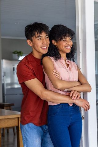 Smiling mixed-race couple embracing and leaning by doorway in cozy modern minimalist kitchen