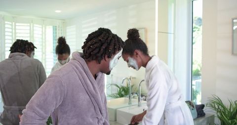 African american couple applying facial masks together in bright modern bathroom
