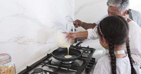 Grandmother and Granddaughter Cooking Pancakes in Modern Kitchen