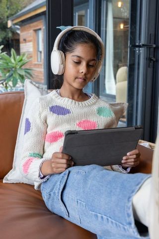 Indian girl using tablet with wireless headphones on cozy living room sofa