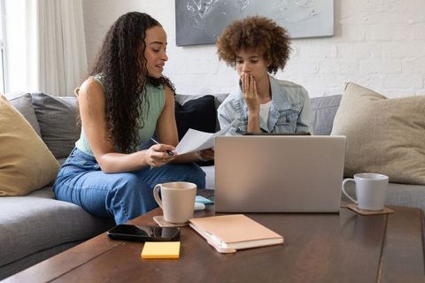 African american women reviewing documents and planning together on sofa with laptop
