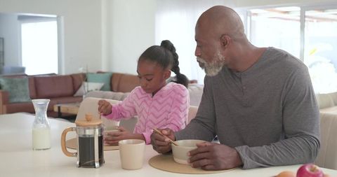 African american grandfather and granddaughter enjoying morning breakfast with coffee