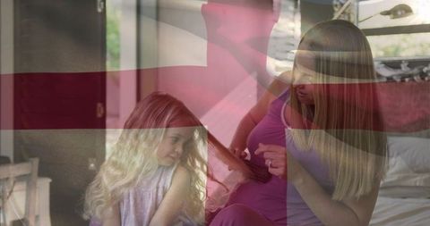 Mother brushing daughter's hair on bed, tender morning bonding with red cross overlay