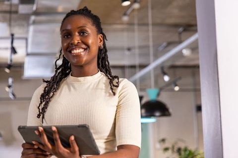 African american woman smiling holding tablet in modern coworking office